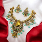 Gold Lakshmi temple necklace and earrings set with mint-green beads and pearls, flat-lay on red satin