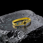 Gold bracelet with a blue gemstone and black design on a textured surface