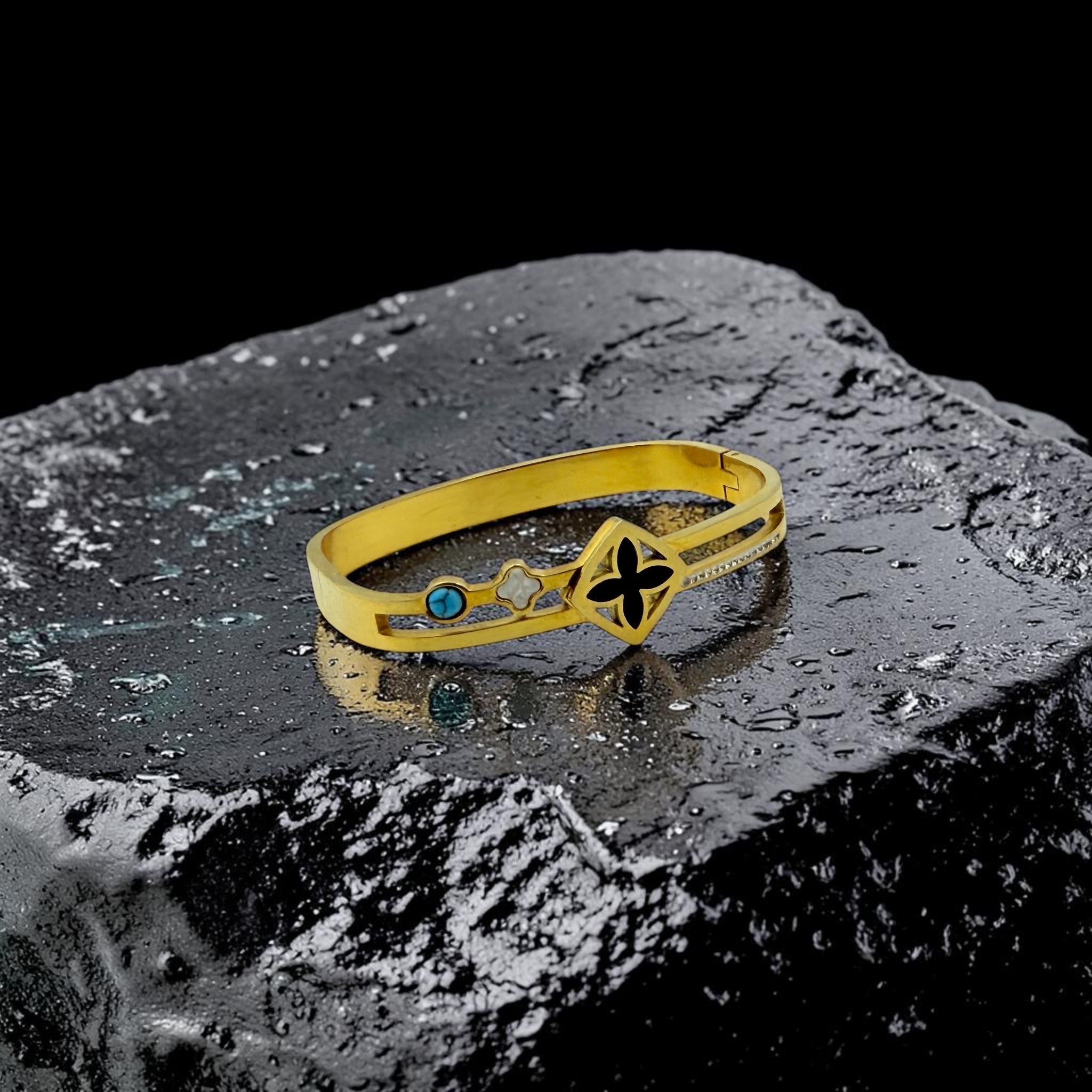 Gold bracelet with a blue gemstone and black design on a textured surface