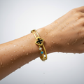 Gold bracelet with a black and blue stone on a wet wrist against a white background