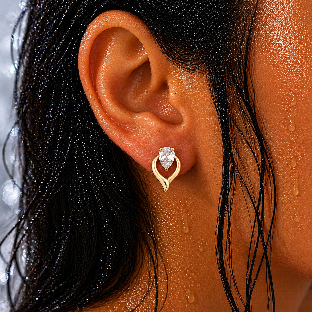 Gold-tone teardrop halo stud earring with pear-cut crystal, close-up on-ear shot