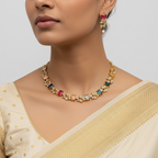 Woman wearing a gold necklace with colorful gemstones on a plain background