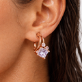 Close-up of a woman's ear wearing a rose gold hoop earring with a purple gemstone.