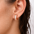 Close-up of an ear wearing a rose gold hoop earring with clear gemstones.