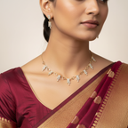 Gold-toned choker necklace with heart charms and pearl tassel drops, worn on-model with a saree