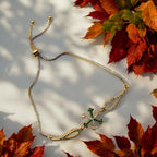 Gold-toned trident bracelet with green and white CZ stones on adjustable chain, worn on wrist poolside