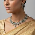 Antique gold-tone floral vine necklace set with clear, green and pink stones, flat-lay on white cushion over autumn leaves