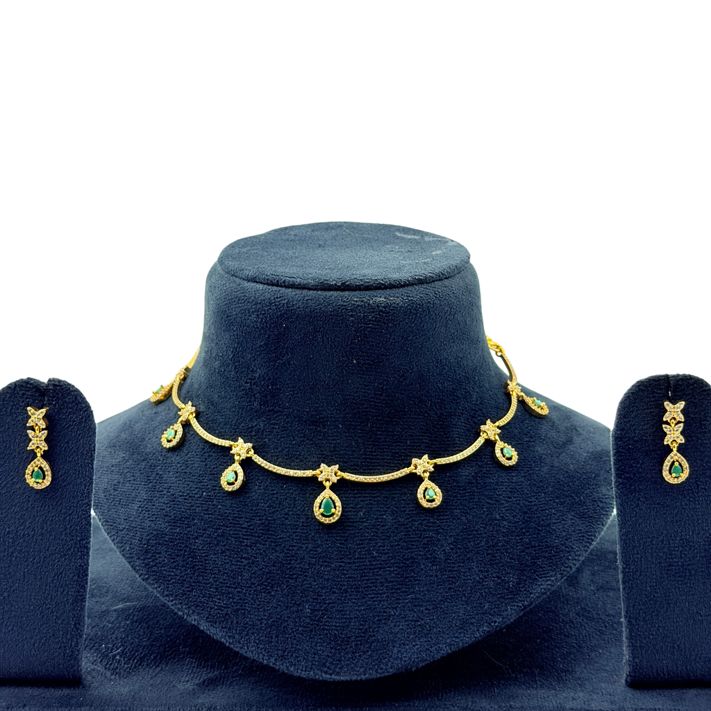 Gold necklace with green gemstones on a blue velvet stand, accompanied by matching earrings.
