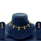 Gold necklace with green gemstones on a blue velvet stand, accompanied by matching earrings.