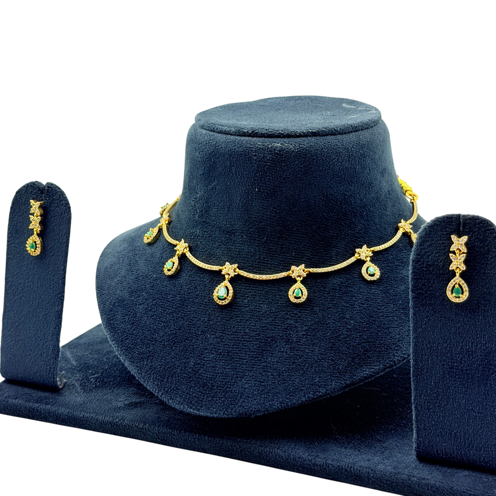 Gold necklace with green gemstones and matching earrings on a blue stand.