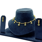 Gold necklace with green gemstones and matching earrings on a blue stand.