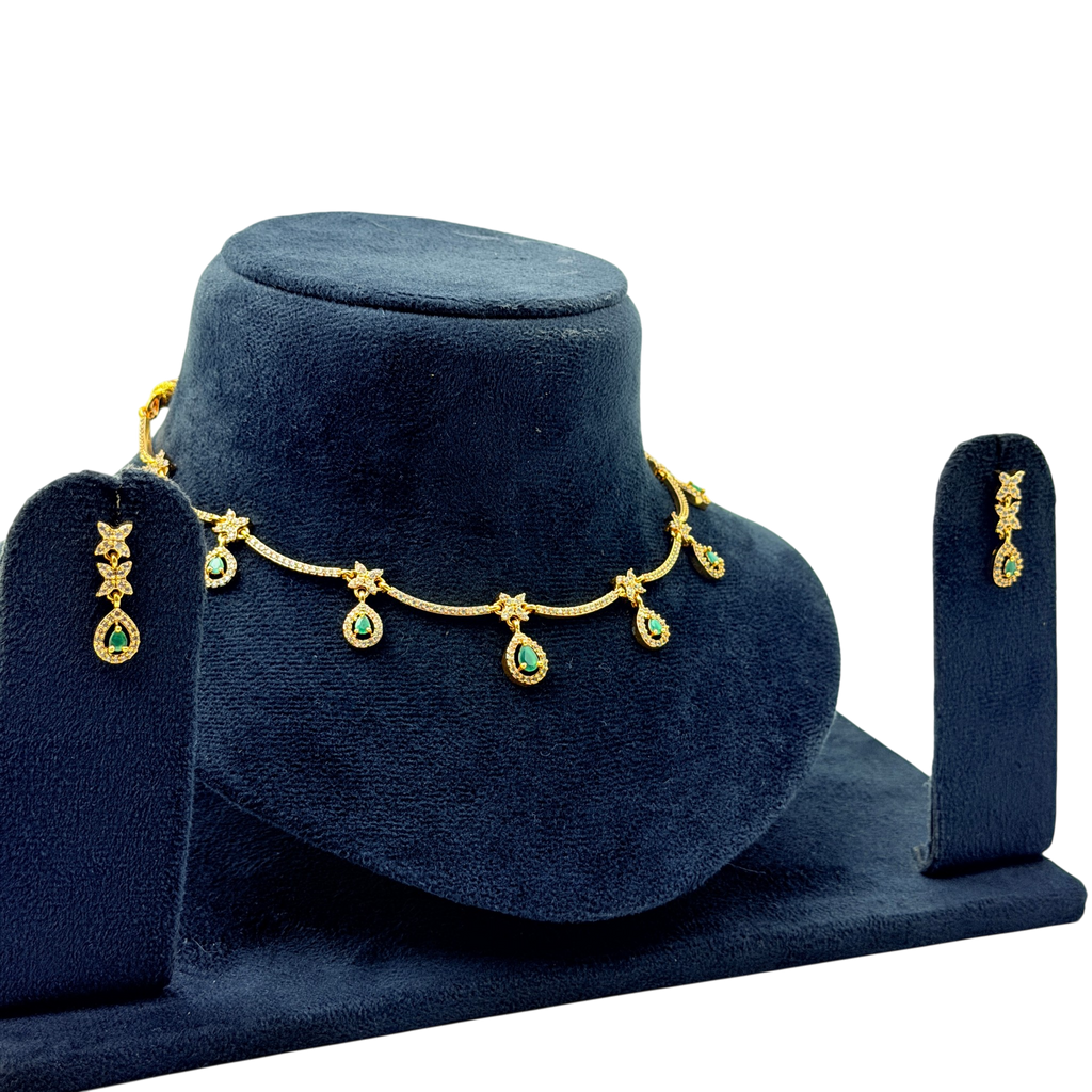Gold necklace with green gemstones on a blue velvet stand, accompanied by matching earrings.