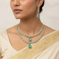 Woman wearing a gold necklace with green gemstones and matching earrings.