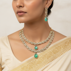 Woman wearing a gold necklace with green gemstones and matching earrings.
