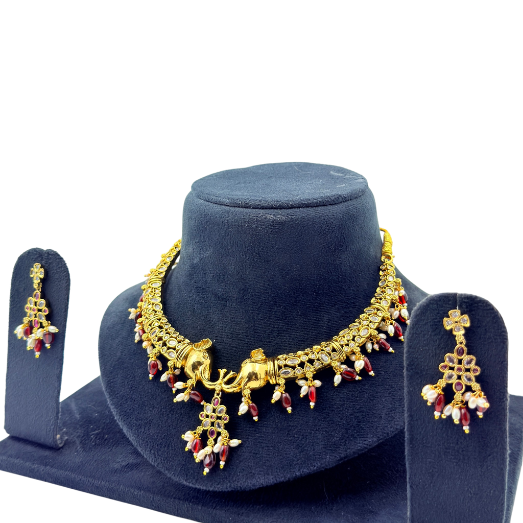 Gold necklace with red and clear stones on a blue stand with matching earrings.
