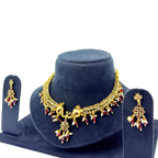 Gold necklace with red and clear stones on a blue stand with matching earrings.