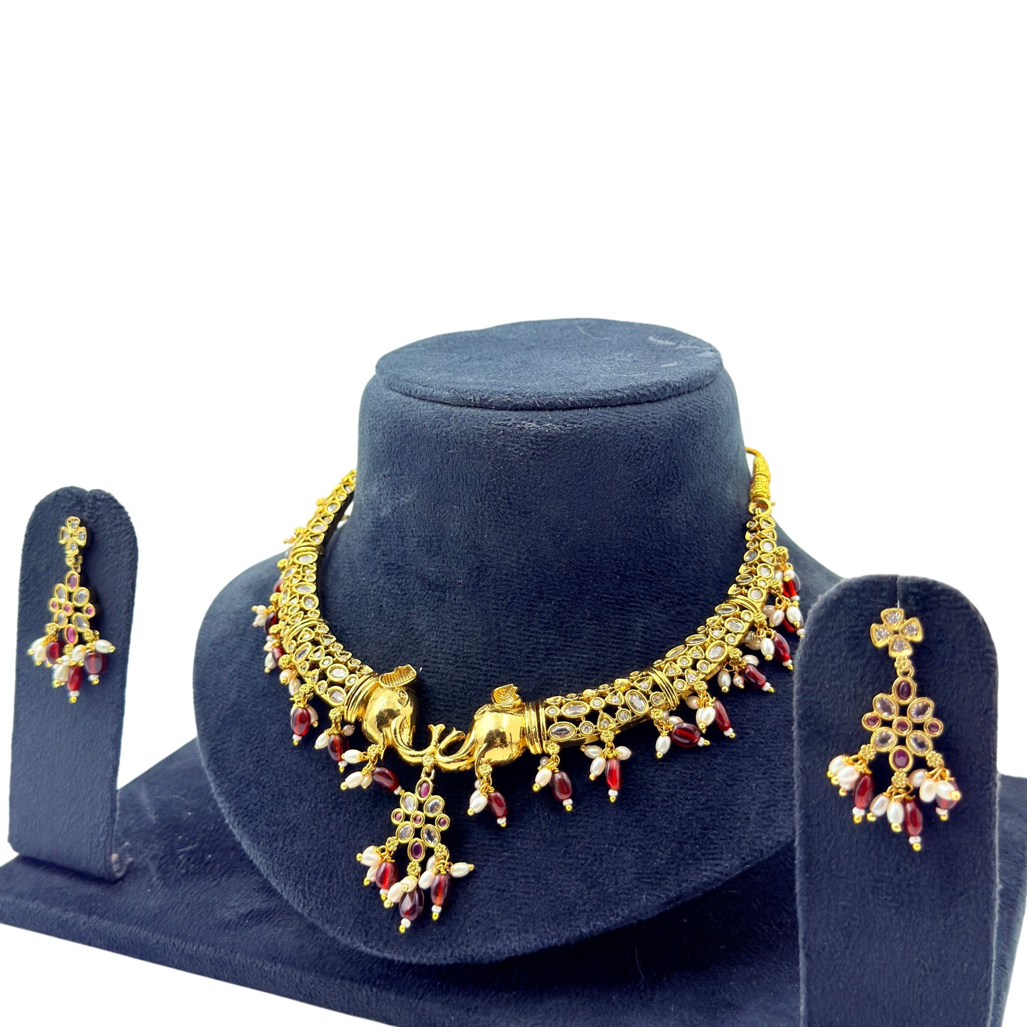 Gold necklace with red and clear stones on a blue stand with matching earrings.