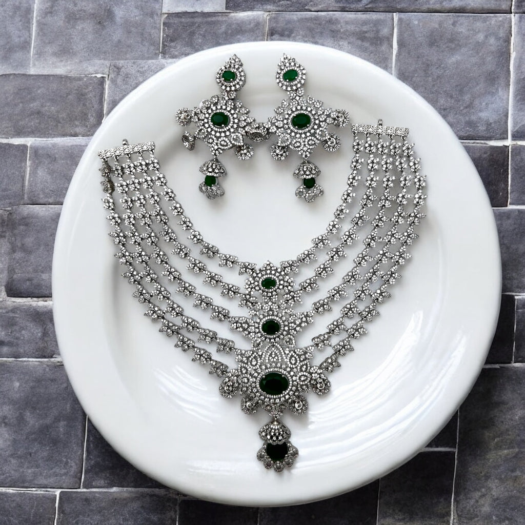 Silver-tone emerald & white stone multi-layered necklace set with earrings, flat-lay on white plate
