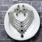 Silver-tone emerald & white stone multi-layered necklace set with earrings, flat-lay on white plate