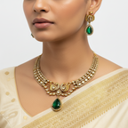 Woman wearing a gold necklace and earrings with green gemstones on a plain background