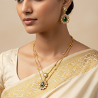 Woman wearing gold jewelry with green gemstones on a beige background