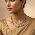 Woman wearing a gold necklace with emerald and diamond accents and matching earrings.