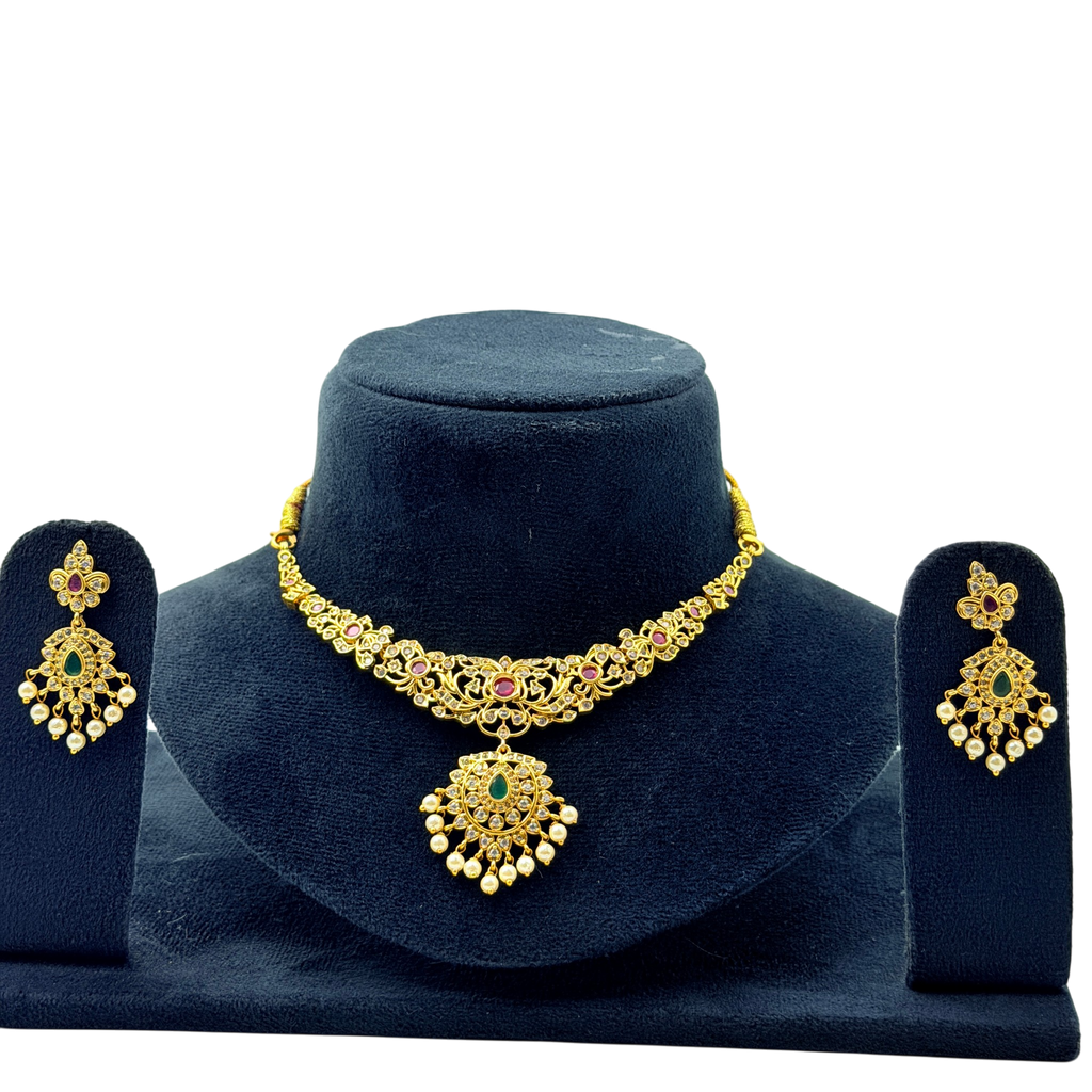 Gold necklace with green and red stones on a dark blue stand, accompanied by matching earrings.