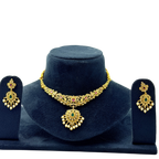 Gold necklace with green and red stones on a dark blue stand, accompanied by matching earrings.