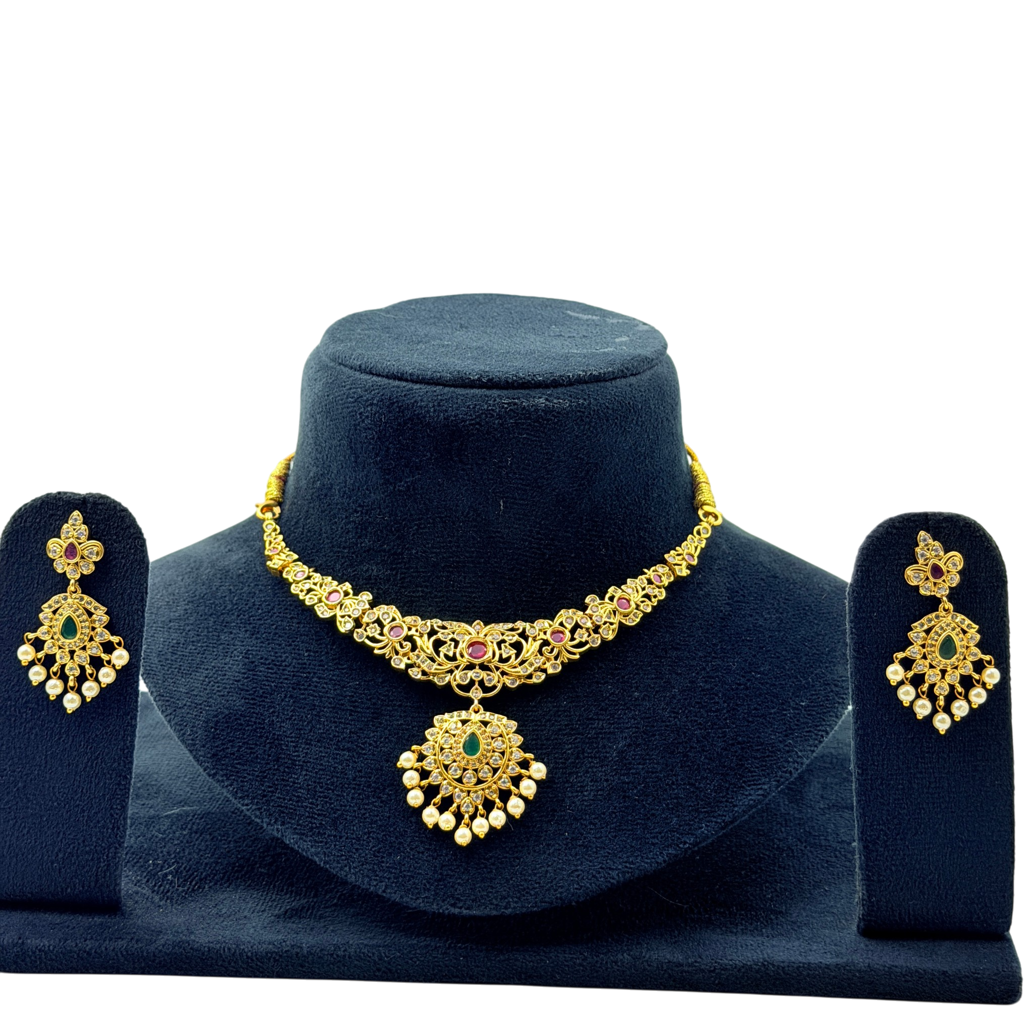 Gold necklace with green and red stones on a dark blue stand, accompanied by matching earrings.