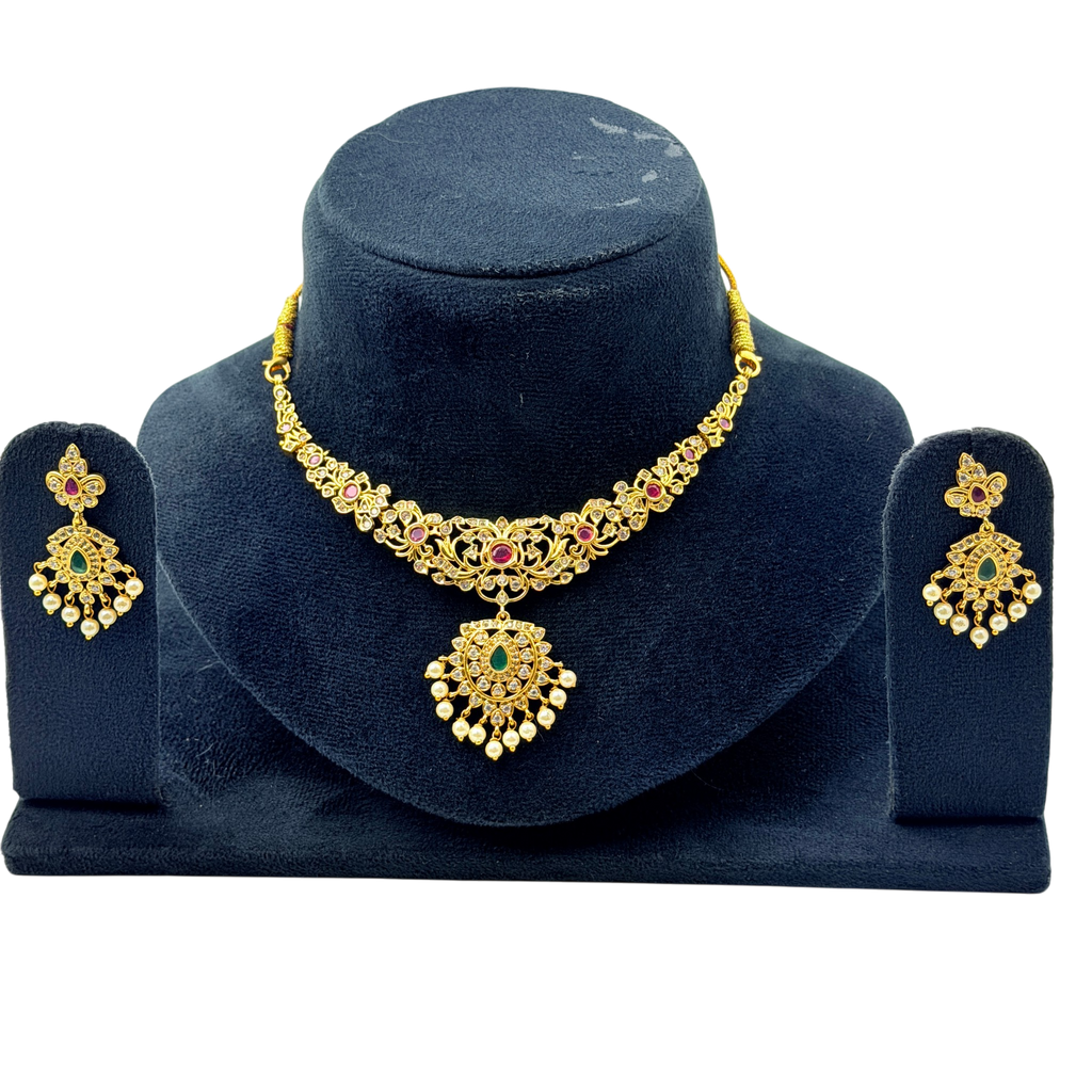 Gold necklace and earrings set on a dark blue stand with a white background
