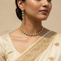 Woman wearing a gold necklace and earrings with a beige saree.