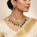 Woman wearing a gold necklace with green gemstones and matching earrings.
