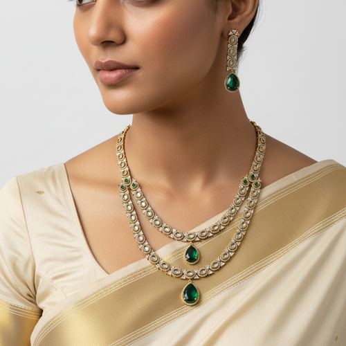 Woman wearing a gold necklace with green gemstones and earrings on a plain background
