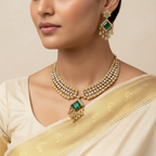 Woman wearing a gold necklace and earrings with green gemstones on a beige background