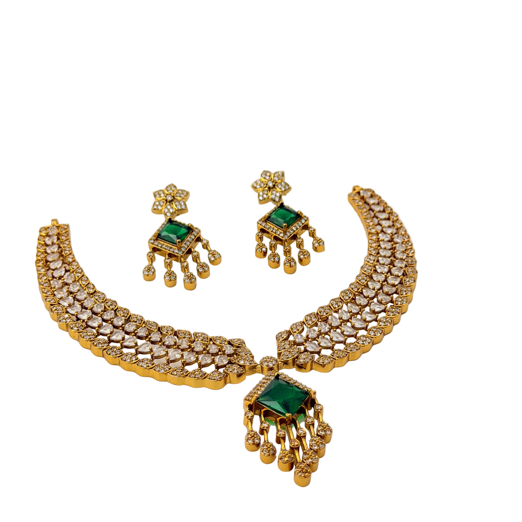 Gold necklace and earrings set with green gemstones on a white background
