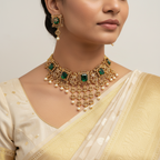 Woman wearing a gold necklace with emeralds and pearls on a plain background