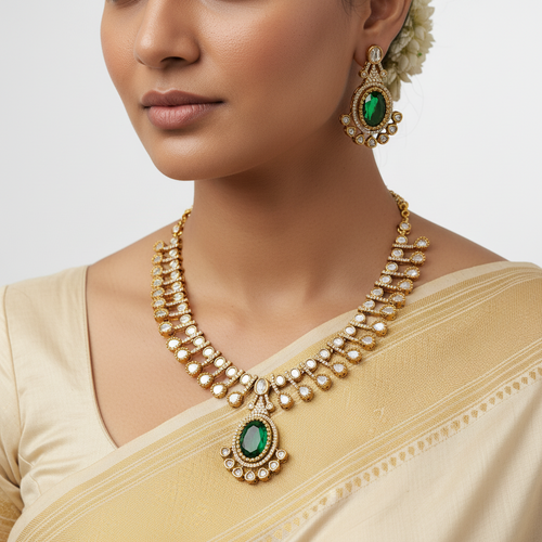 Woman wearing a gold necklace and earrings with green gemstones on a plain background