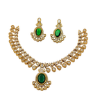 Gold necklace and earrings set with green gemstones on a white background