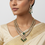 Woman wearing a gold necklace with green gemstones and matching earrings on a plain background