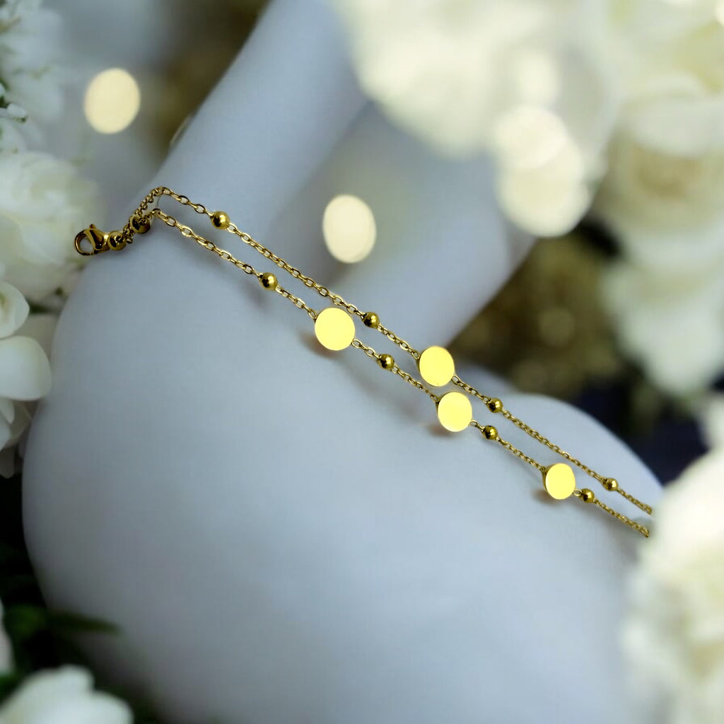 Gold-toned double chain bracelet with beads and polished disc charms, worn on wrist