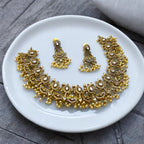 Antique gold Kundan necklace and earrings set with white stones and pearl fringe, flat-lay on a white plate