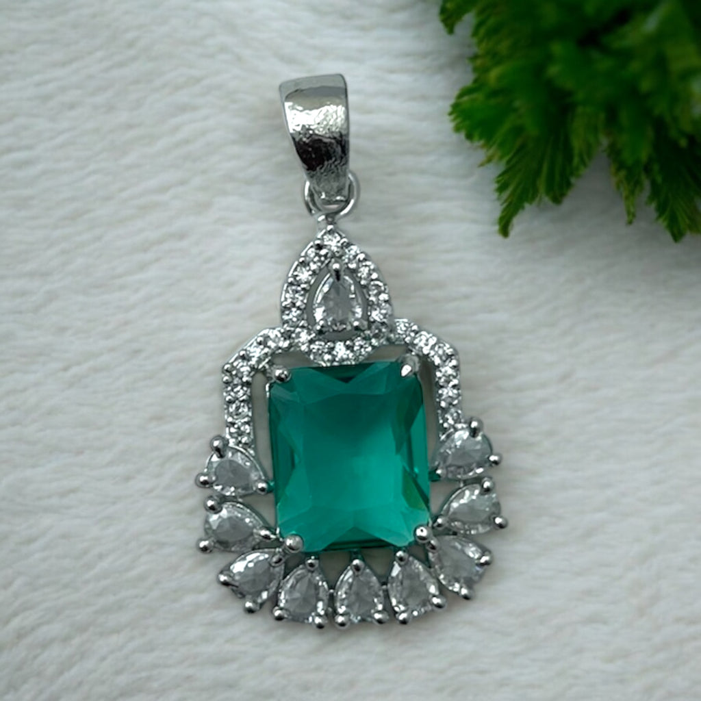 Silver-tone green emerald-cut halo pendant with clear pear-shaped CZ accents, flat-lay close-up