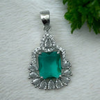 Silver-tone green emerald-cut halo pendant with clear pear-shaped CZ accents, flat-lay close-up