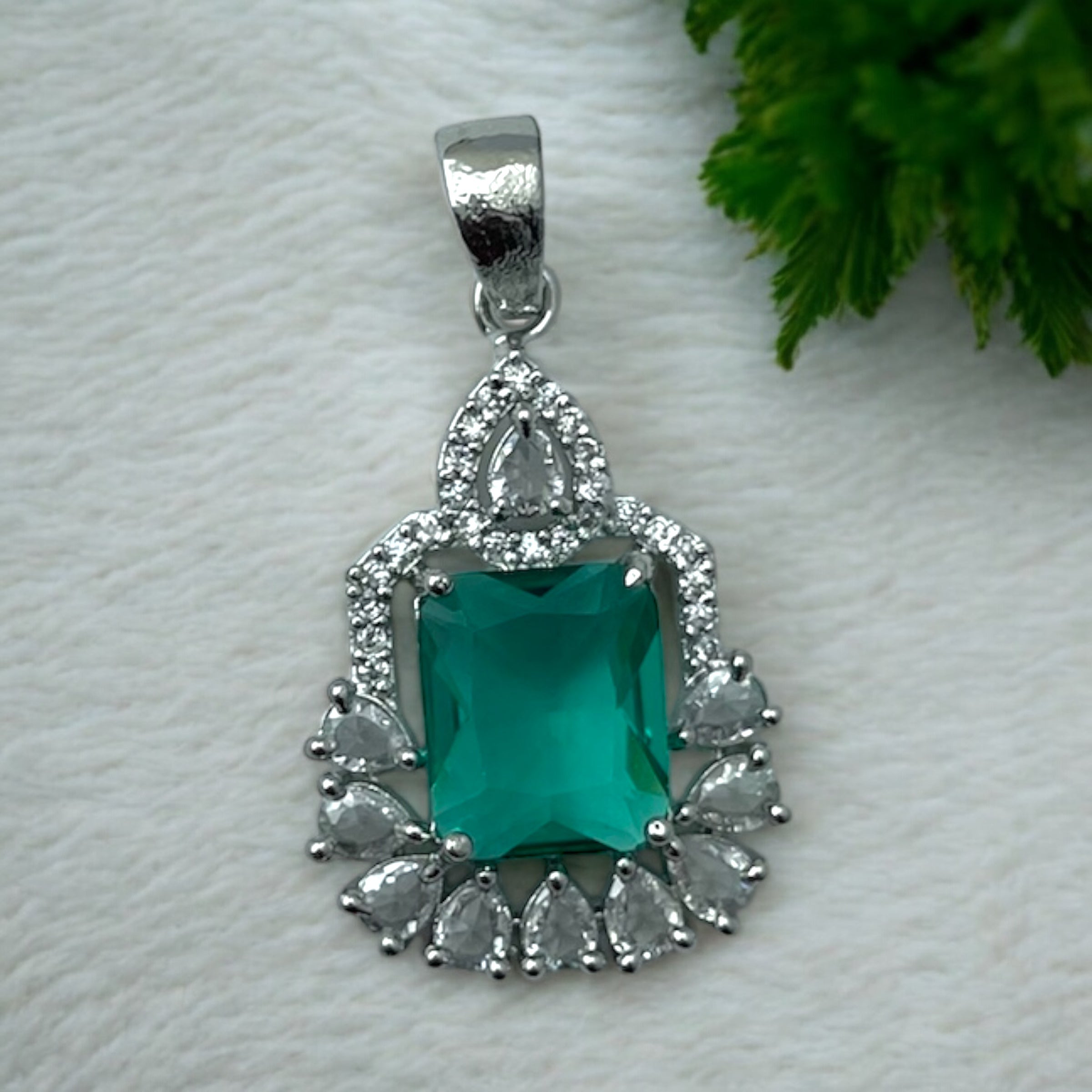 Silver-tone green emerald-cut halo pendant with clear pear-shaped CZ accents, flat-lay close-up