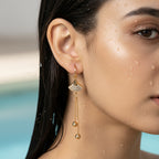 Gold-tone fan motif crystal tassel earrings on model's ear, close-up on-ear shot