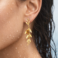 Close-up of a person wearing a golden leaf earring with a blurred background