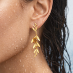 Gold-tone floral branch dangle earring with 3D rose accent, close-up on-ear shot