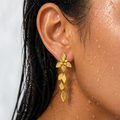 Close-up of a person wearing gold leaf earrings with a blurred background