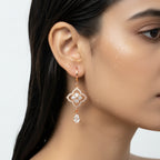 Rose gold floral clover drop earrings with CZ teardrop charm, worn on ear close-up