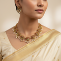 Woman wearing a gold and pearl necklace with a beige saree on a neutral background